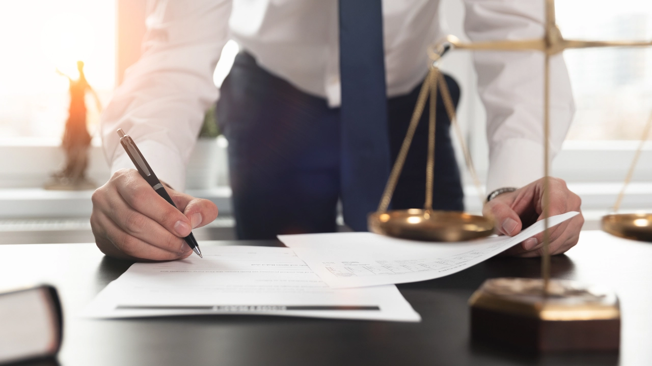 Ein Anwalt unterschreibt Dokumente, im Vordergrund steht eine Richterwaage