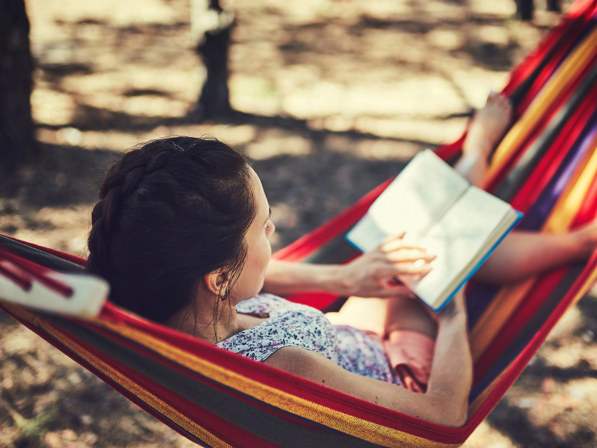 Junge Frau liegt in einer Hängematte und liest ein Buch